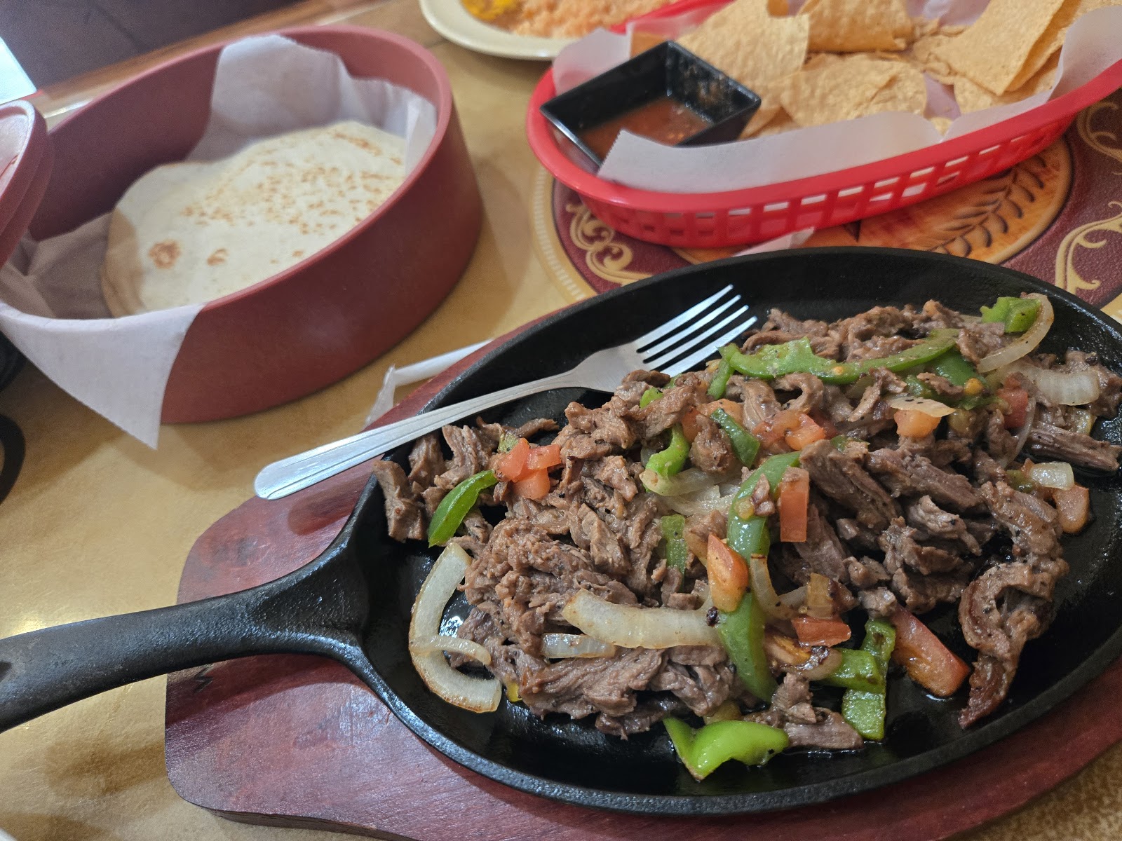 Sizzling beef fajitas on a cast-iron skillet with tortillas and chips